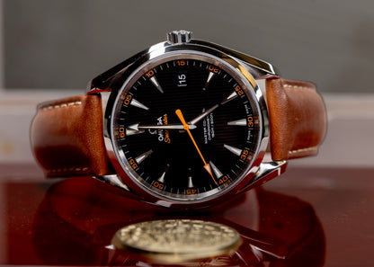 Omega Seamaster Aqua Terra 150M watch with brown leather strap and black dial, displayed on a wooden surface.