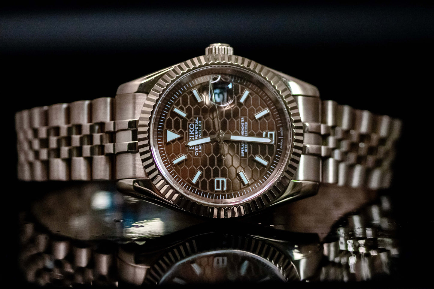Seiko Mod Rose Gold Land Dweller watch with chocolate dial and rose gold case on a reflective surface.