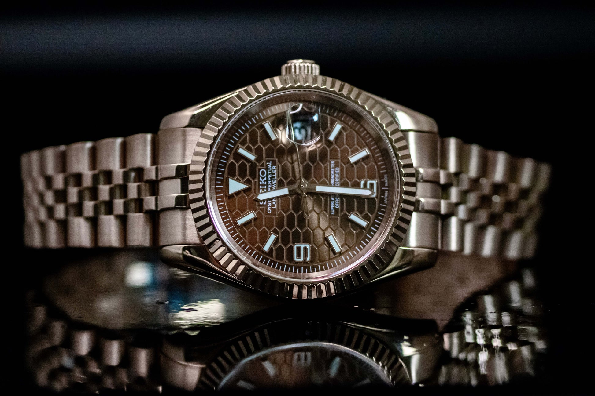 Seiko Mod Rose Gold Land Dweller watch with chocolate dial and rose gold case on a reflective surface.