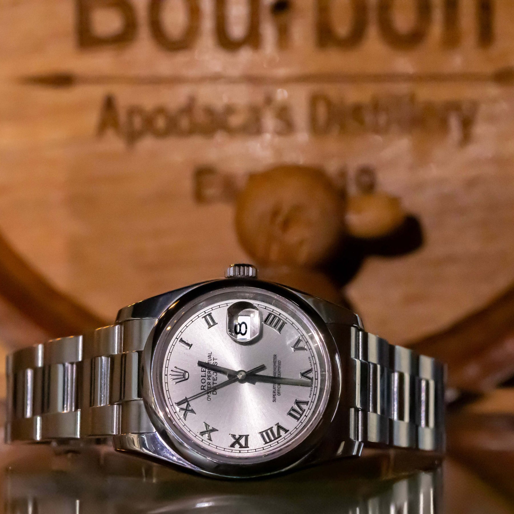 Rolex Datejust 36 full set displayed on a reflective surface with a bourbon barrel backdrop.