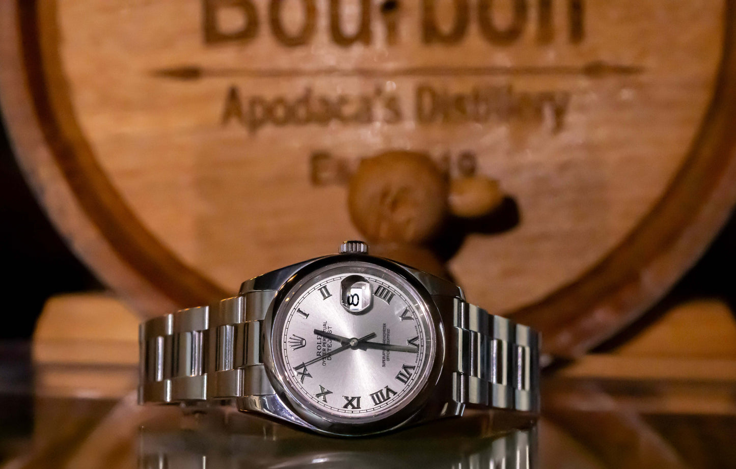 Rolex Datejust 36 full set displayed on a reflective surface with a bourbon barrel backdrop.