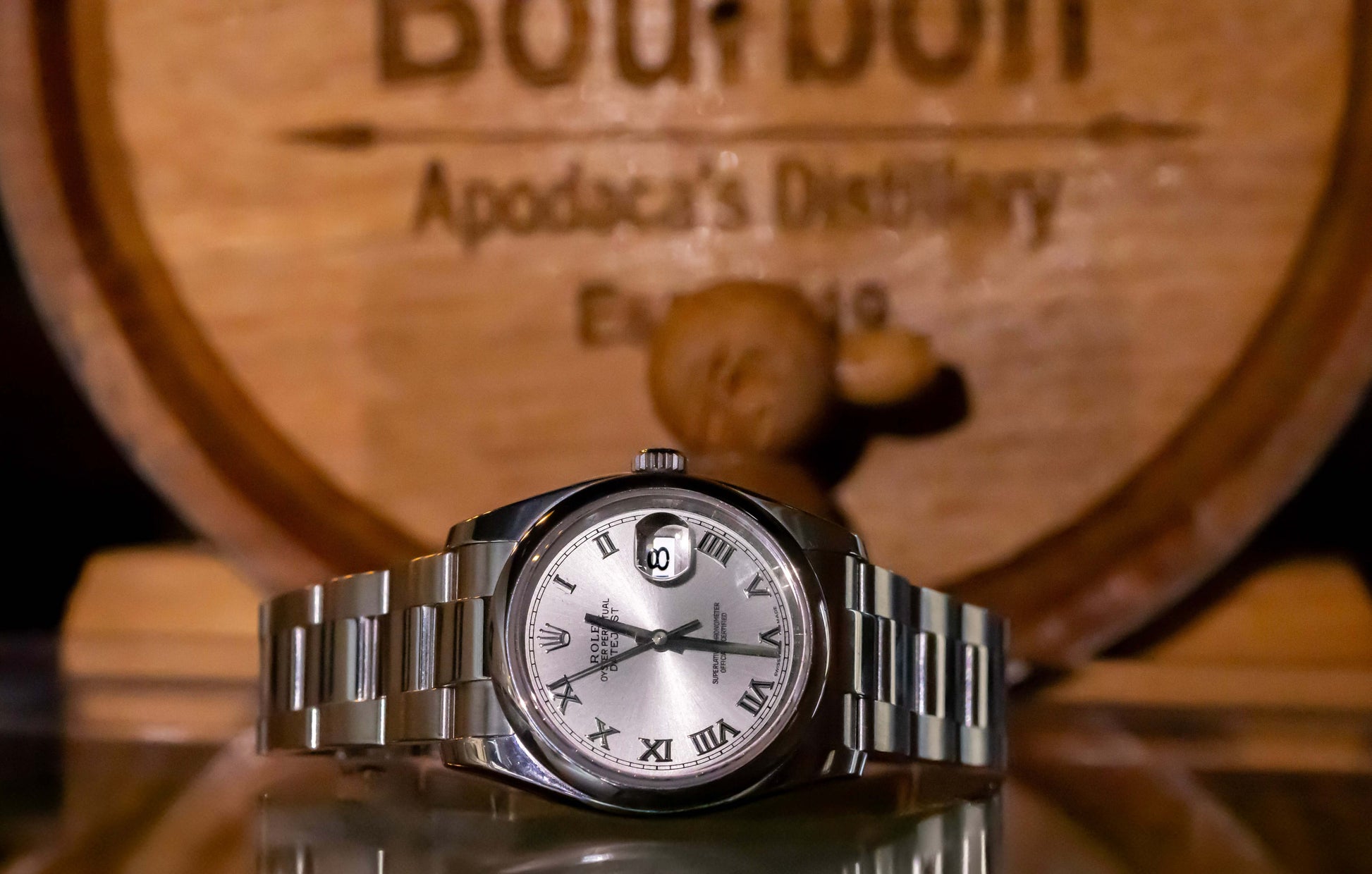 Rolex Datejust 36 full set displayed on a reflective surface with a bourbon barrel backdrop.