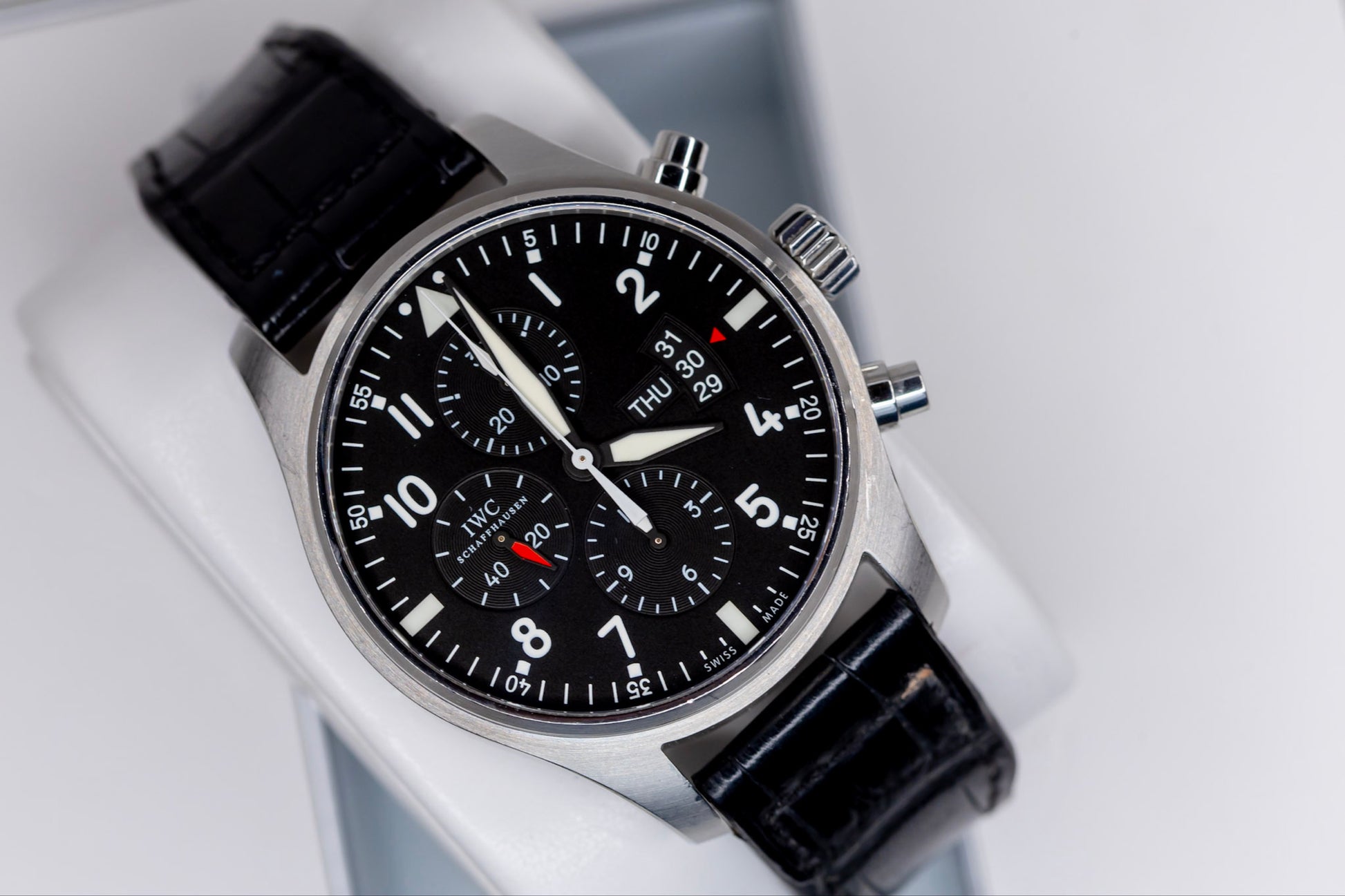 IWC Pilots Watch Chronograph displayed on a black leather strap, showcasing its sleek design and intricate dial features.