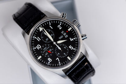 IWC Pilots Watch Chronograph displayed on a black leather strap, showcasing its sleek design and intricate dial features.