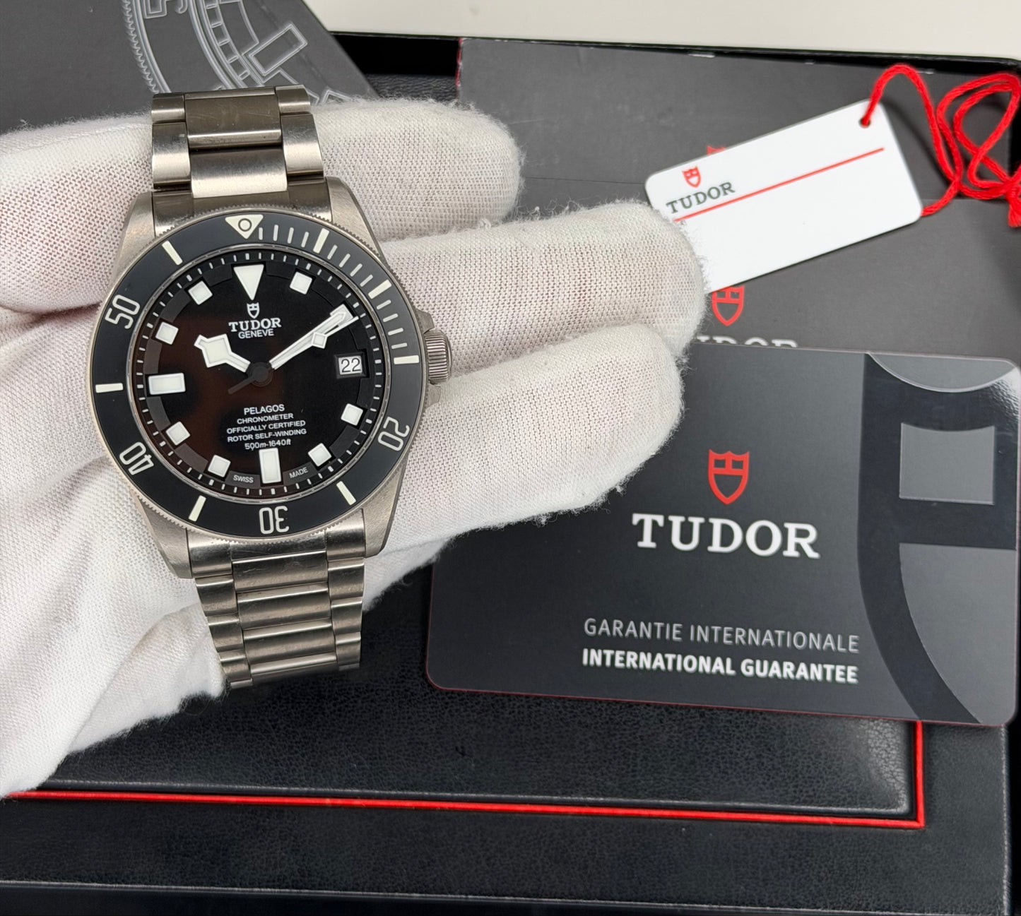 Tudor Pelagos dive watch displayed with a titanium case and bracelet, featuring a black dial and international guarantee card.