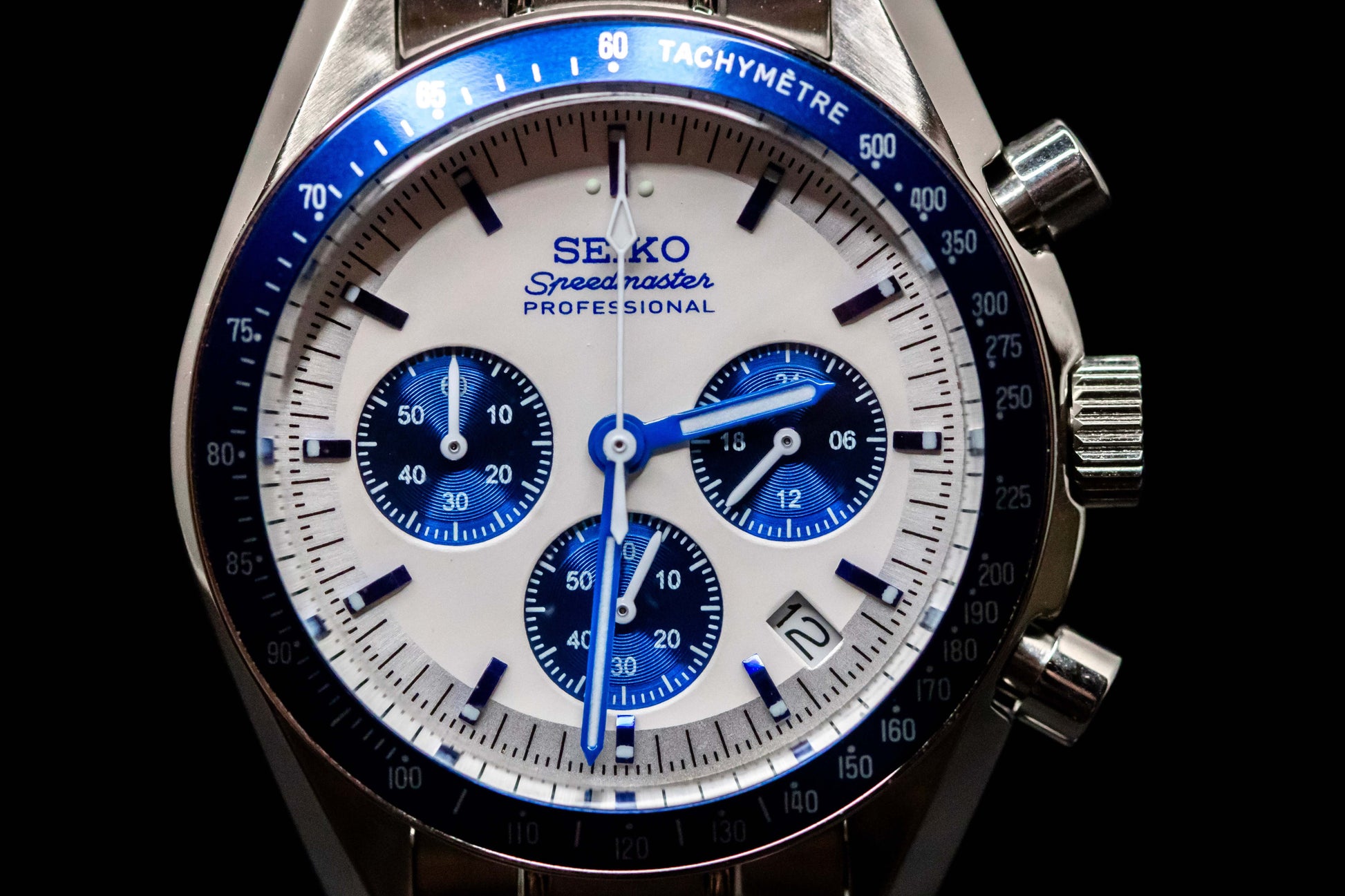 Close-up of Seiko Speedmaster Snoopy watch showing white dial, blue accents, and stainless steel case.