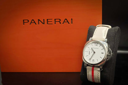 Panerai watch with white strap displayed on a cushion next to the Panerai box.
