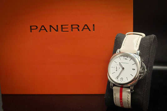Panerai watch with white strap displayed on a cushion next to the Panerai box.