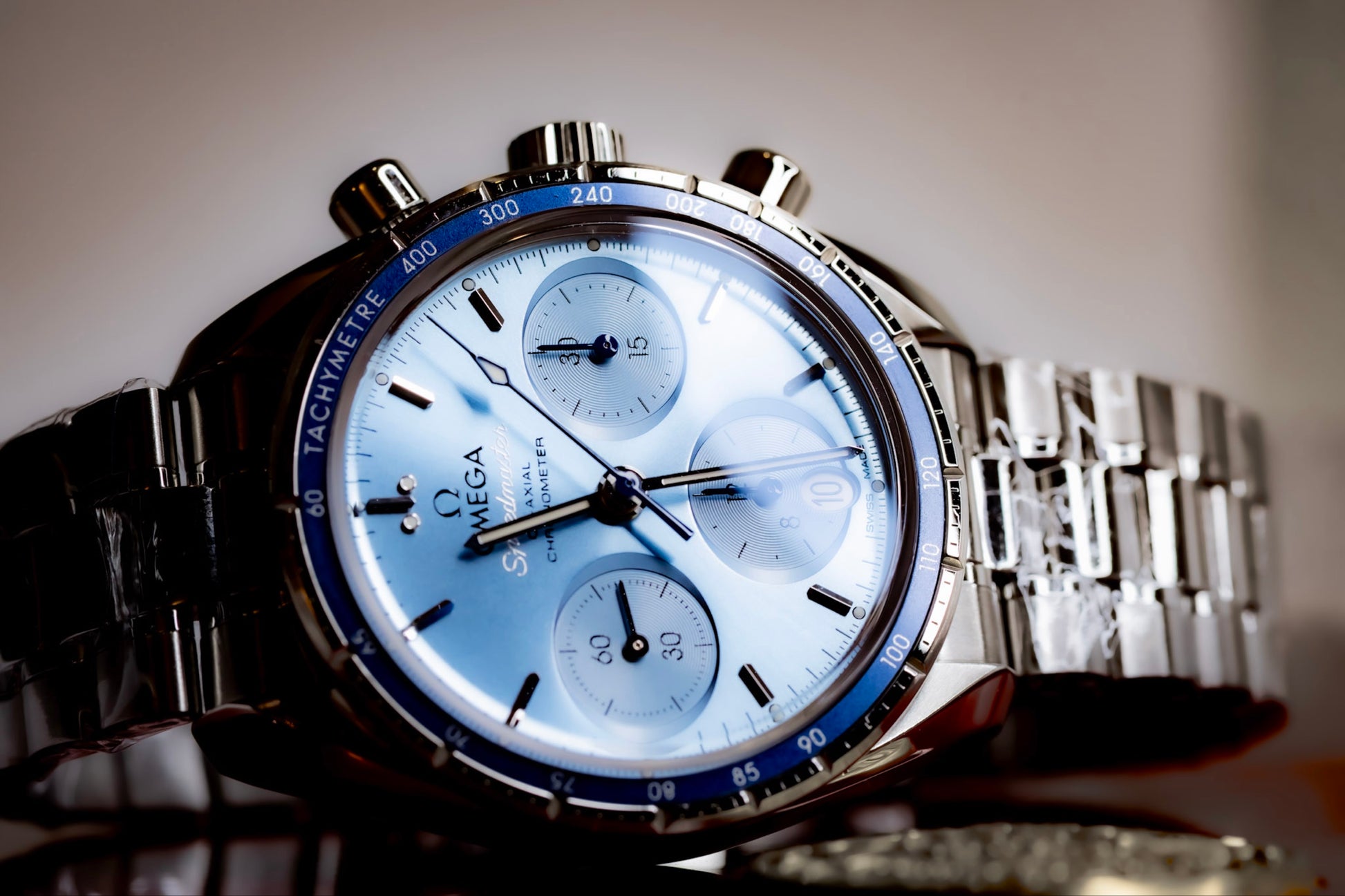 Omega Speedmaster 38mm blue dial chronograph with polished stainless steel bracelet and blue tachymetric bezel.