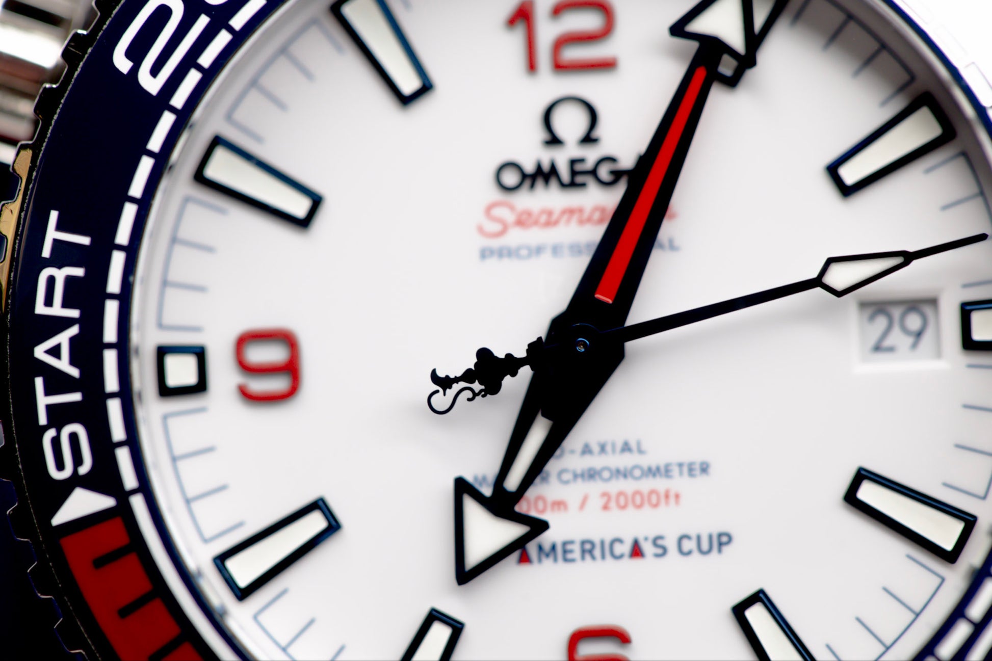 Close-up of Omega Seamaster America's Cup watch dial, showcasing white face, red and blue accents, and automatic movement.