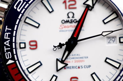 Close-up of Omega Seamaster America's Cup watch dial, showcasing white face, red and blue accents, and automatic movement.