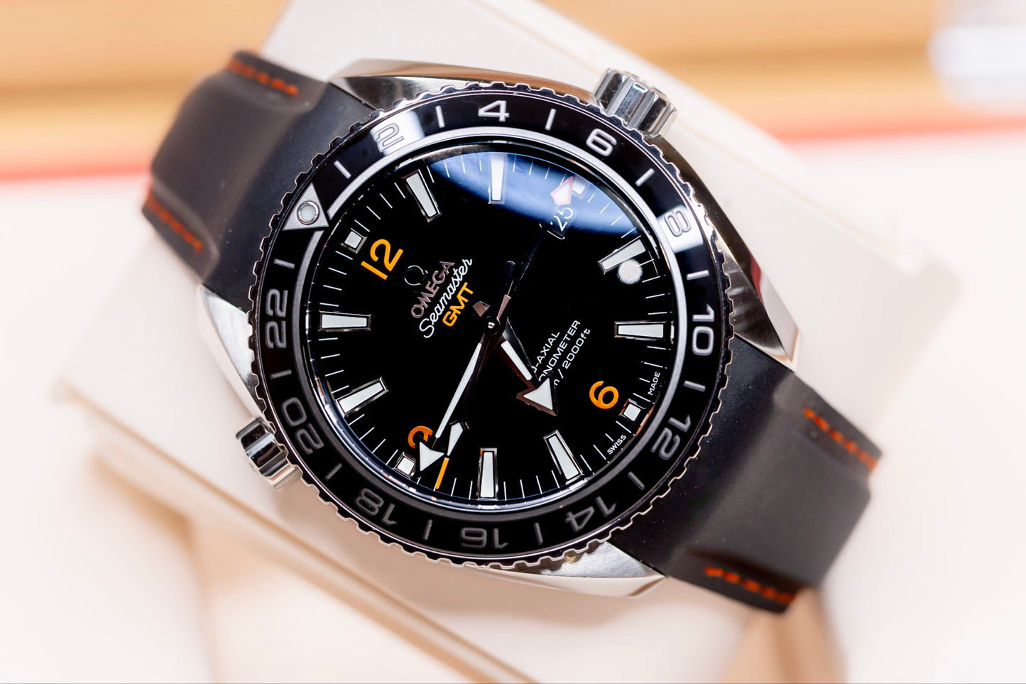 2024 Omega Seamaster Planet Ocean GMT watch on display with black strap and vibrant orange accents.